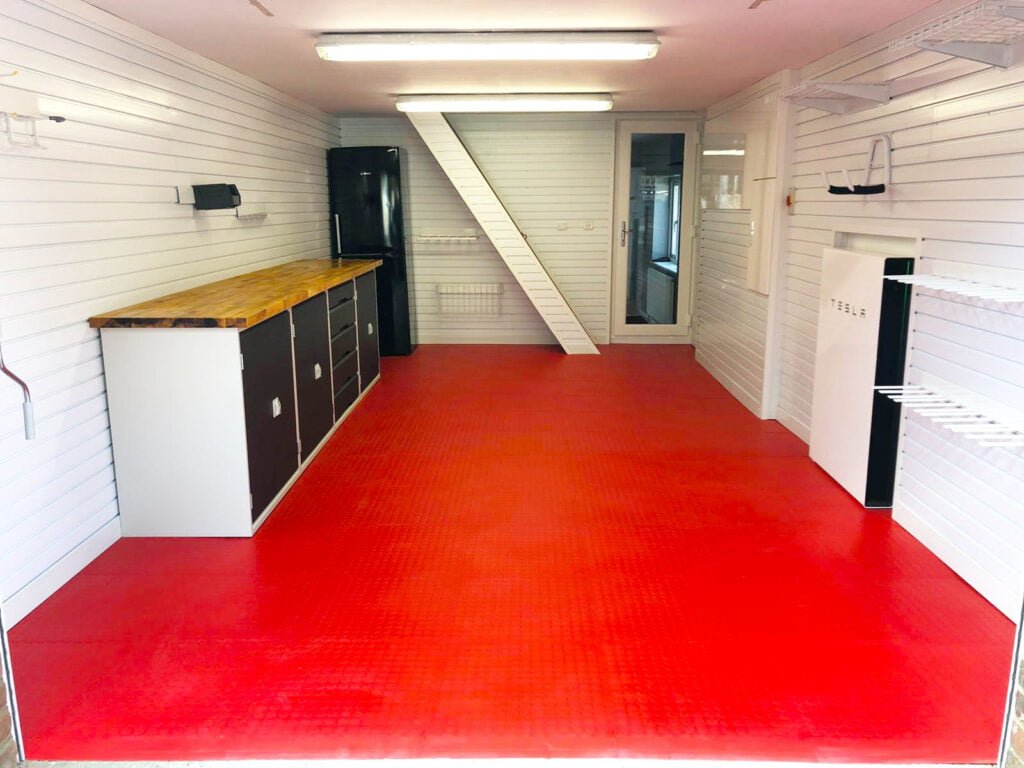 An expertly crafter & modern garage space with a red floor, countertop space and racking.