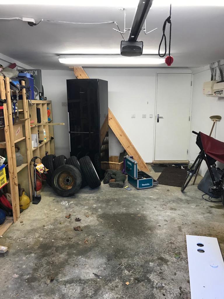 The inside of a garage with broken wooden racking, a refrigerator and old car tyres.