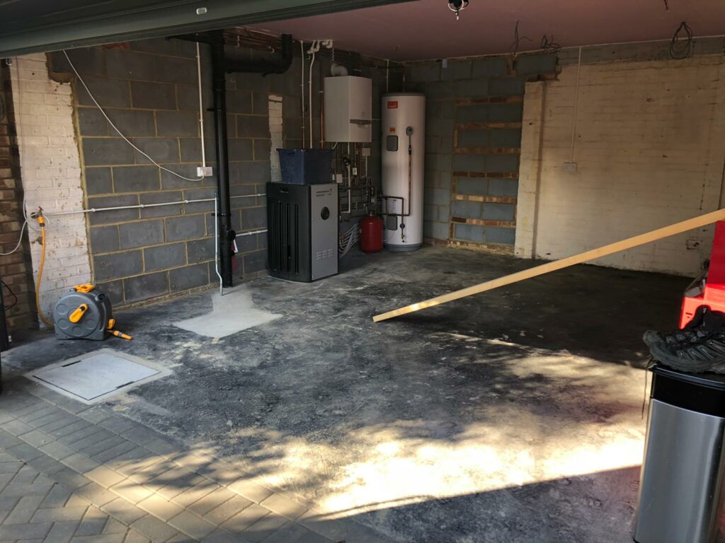 The inside of an empty garage with exposed pipes and a boiler.