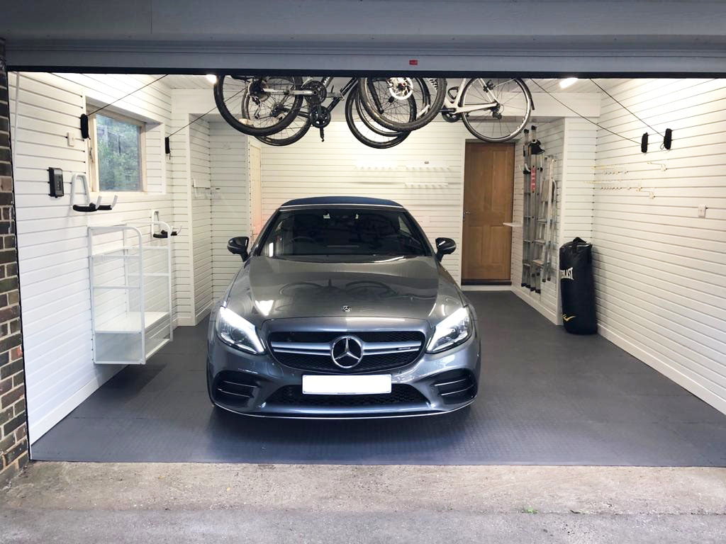 A garage with white walls with shelving, a bike storage rack and a car in the middle of the room.