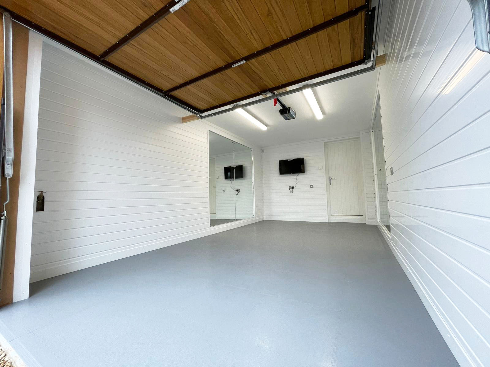 A garage studio conversion with white walls, gym mirrors on the back left wall and a tv on the back wall.