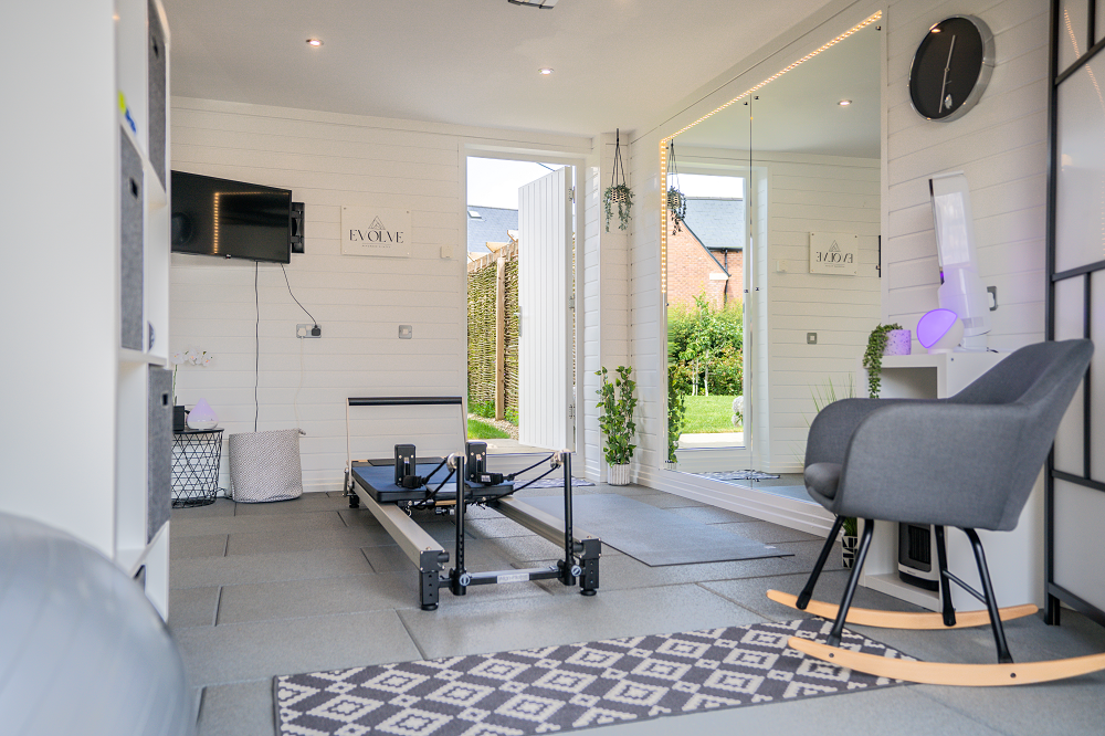 a light and airy garage conversion with an exercise machine, wall-mounted tv, storage and yoga mats on the floor.